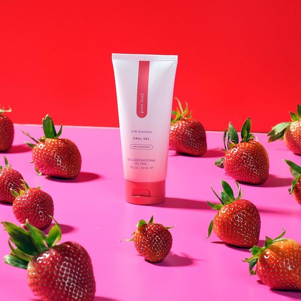 Strawberry oral gel tube on pink surface surrounded by fresh strawberries, red background