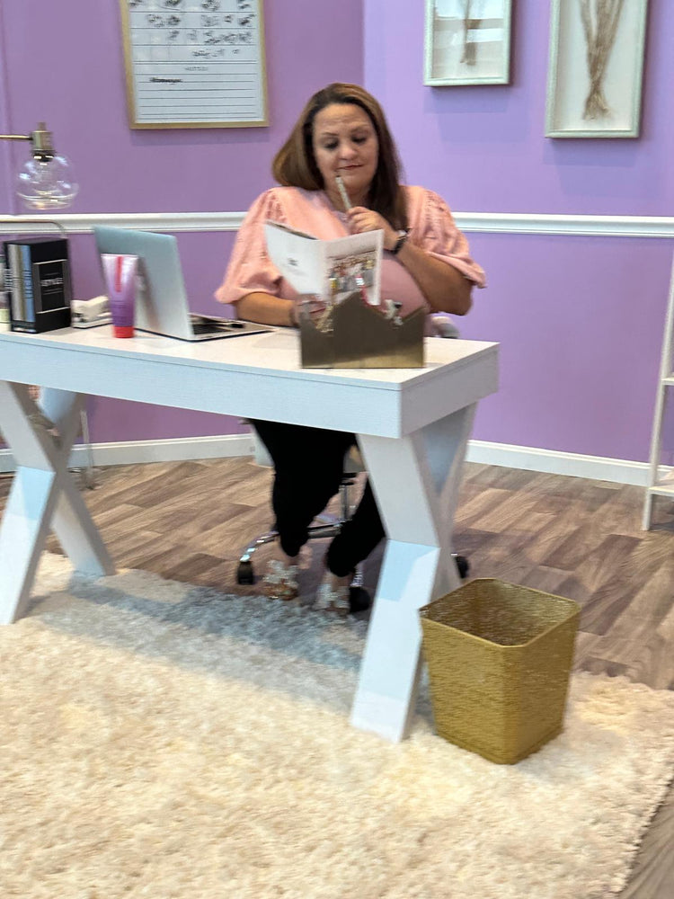 Woman at modern white desk with laptop, reading documents in pastel office setting