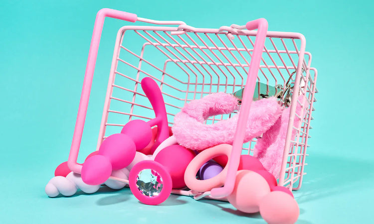 Assorted pink adult wellness products and fluffy handcuffs in a pastel shopping basket