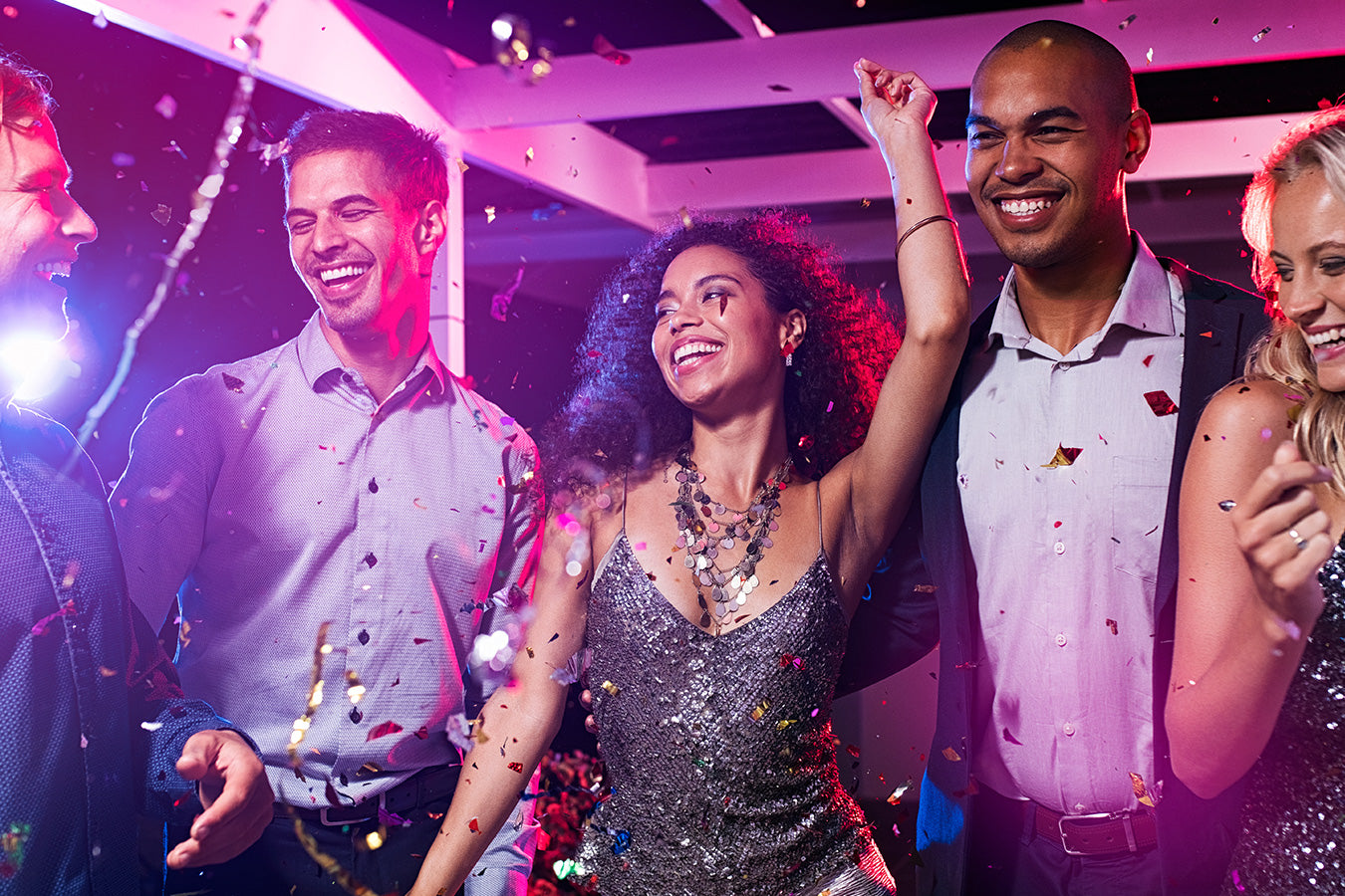 Group of friends celebrating at a festive party with confetti and colorful lights