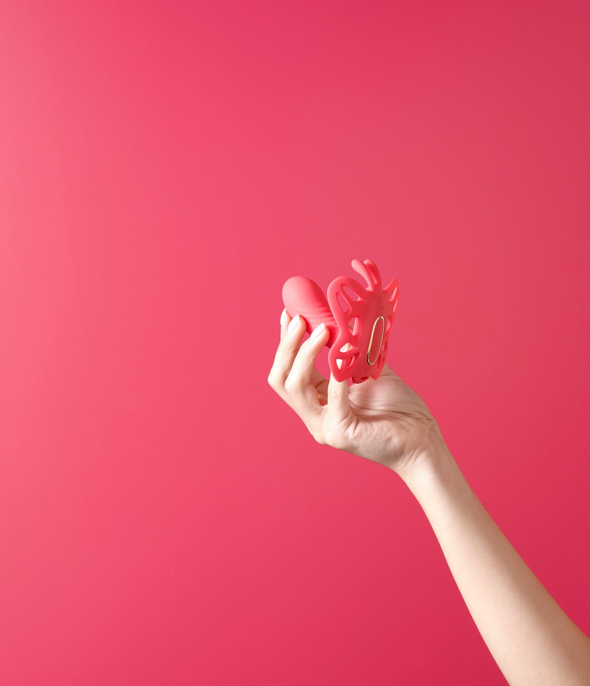 Hand holding a pink silicone butterfly-shaped massage device against a pink background