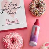Pink skincare serum bottle with donuts and a love note on a pink background