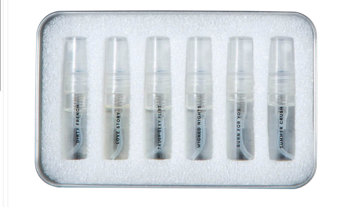 Set of six travel-size perfume sample sprays in clear plastic vials with labeled names in a foam tray