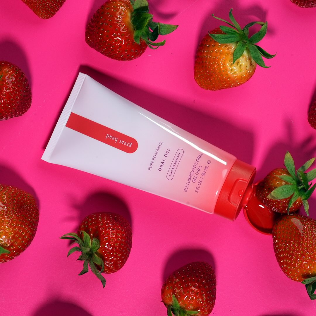 Strawberry-flavored oral gel tube on pink background with fresh strawberries, sensual wellness product.