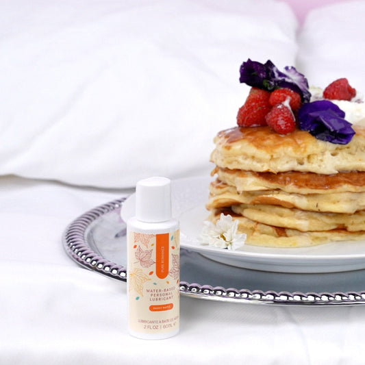 Water-based personal lubricant bottle beside stack of pancakes with berries and edible flowers