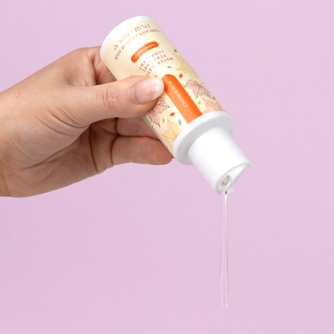 Hand pouring clear liquid from a bottle labeled water-based lubricant on pink background