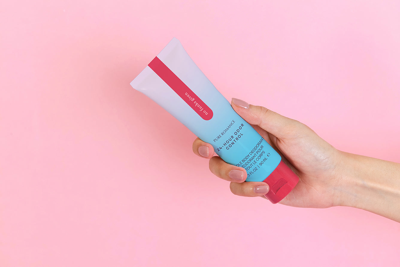 Hand holding a tube of 24-hour odor control body deodorant on a pink background.