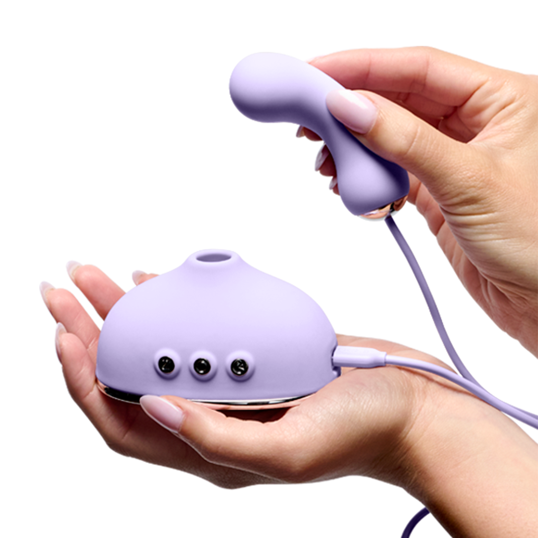 Hands holding a purple silicone massager device with control buttons and a curved attachment