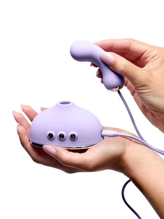 Hands holding a purple silicone wellness massager with control buttons and a wired attachment