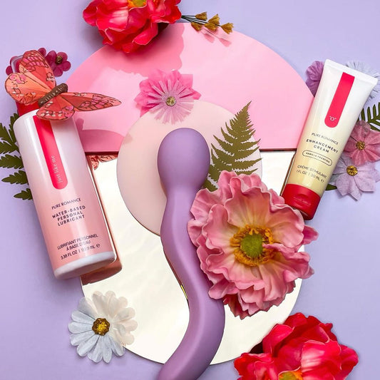 Purple personal massager, water-based lubricant, enhancement cream, and flowers on pastel background