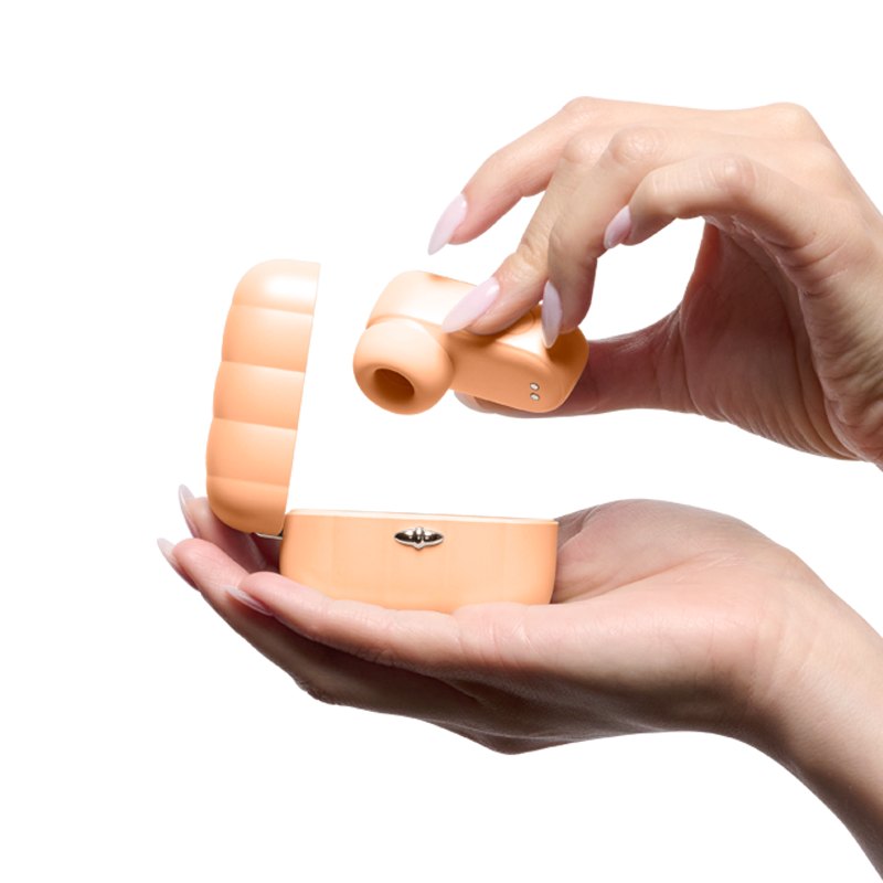 Hand holding orange compact wellness massager with lid open, isolated on white background