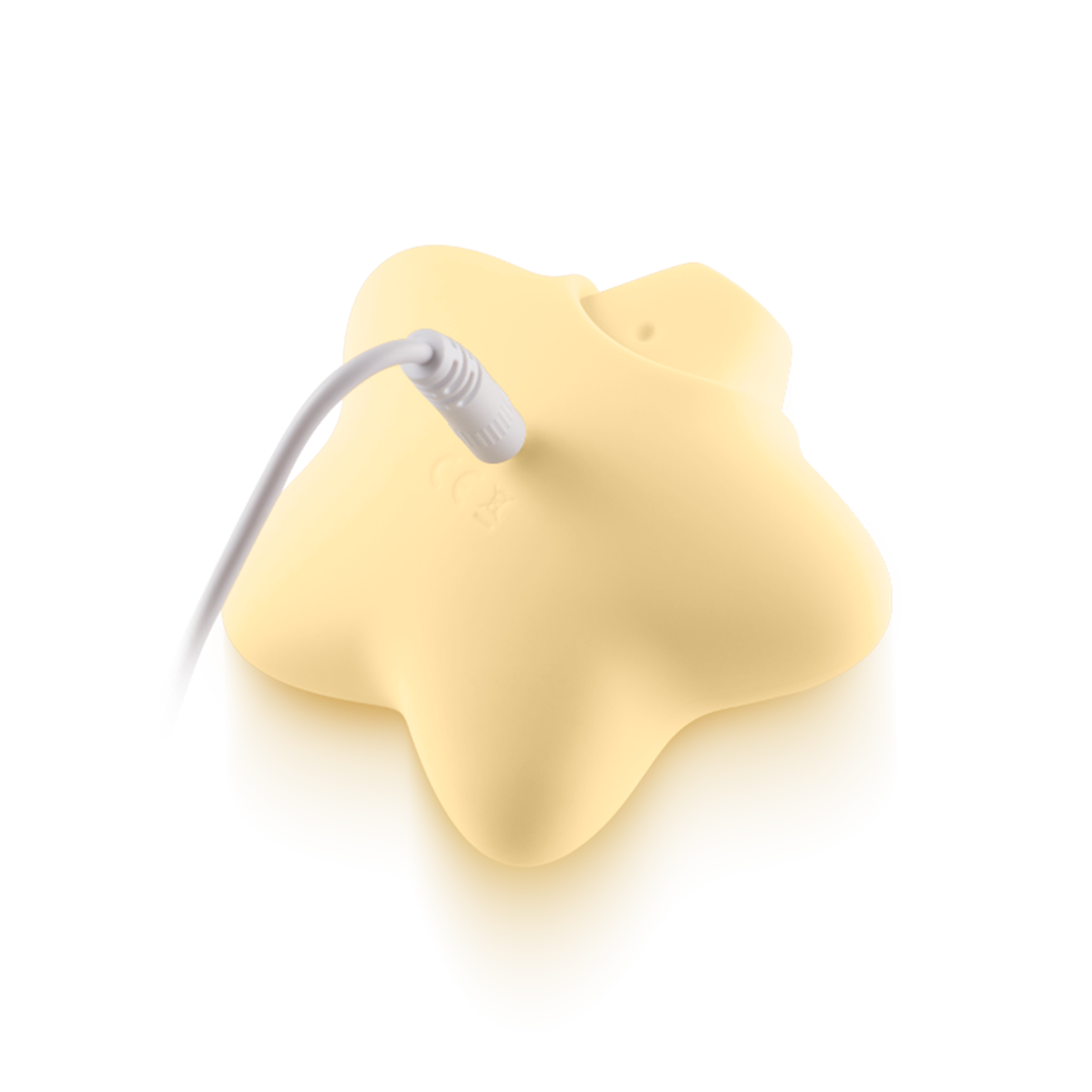 Yellow star-shaped silicone massager charging with white cable on neutral background