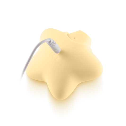 Yellow star-shaped silicone massager charging with white cable on neutral background