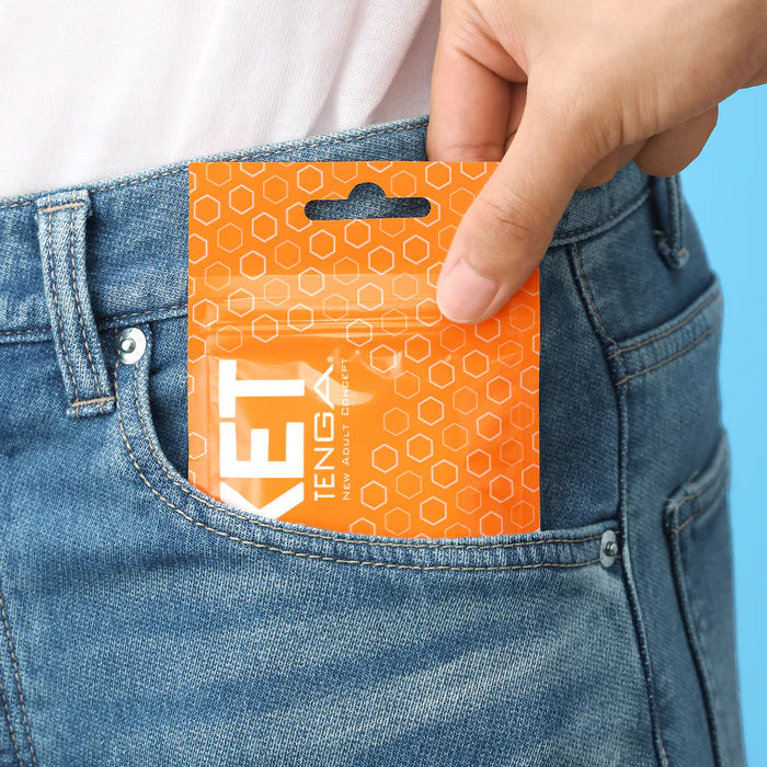 Hand placing orange pocket-size TENGA adult wellness product pouch into denim jeans pocket