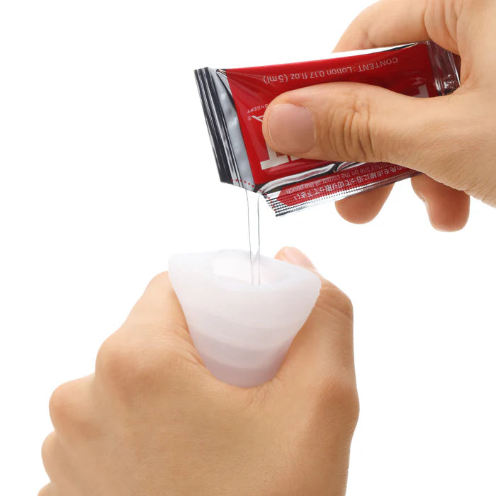 Hand pouring clear gel or lubricant from packet into soft silicone cup