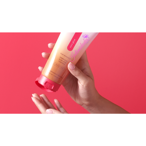 Hands applying tropical flavored massage lotion from a tube against a pink background
