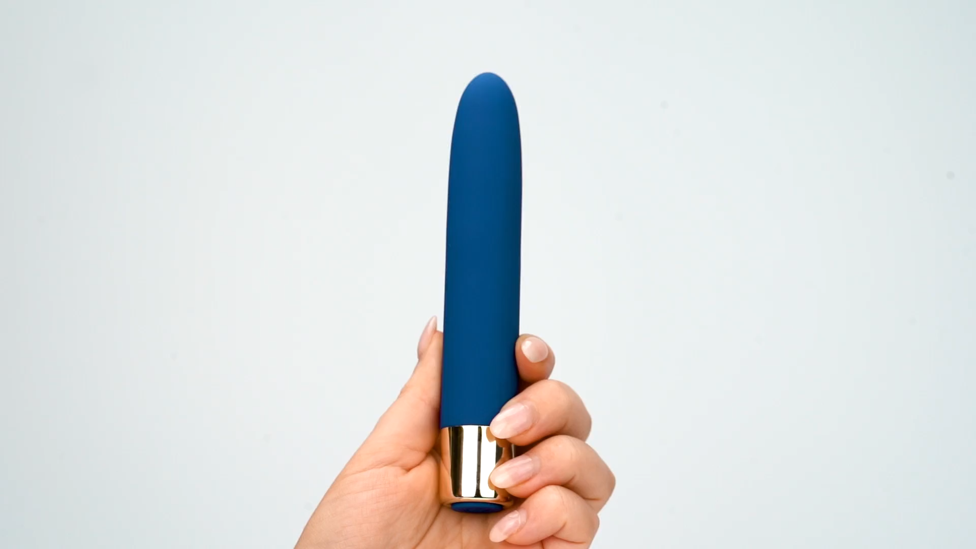 Hand holding a blue silicone personal massager with a gold base on a plain background